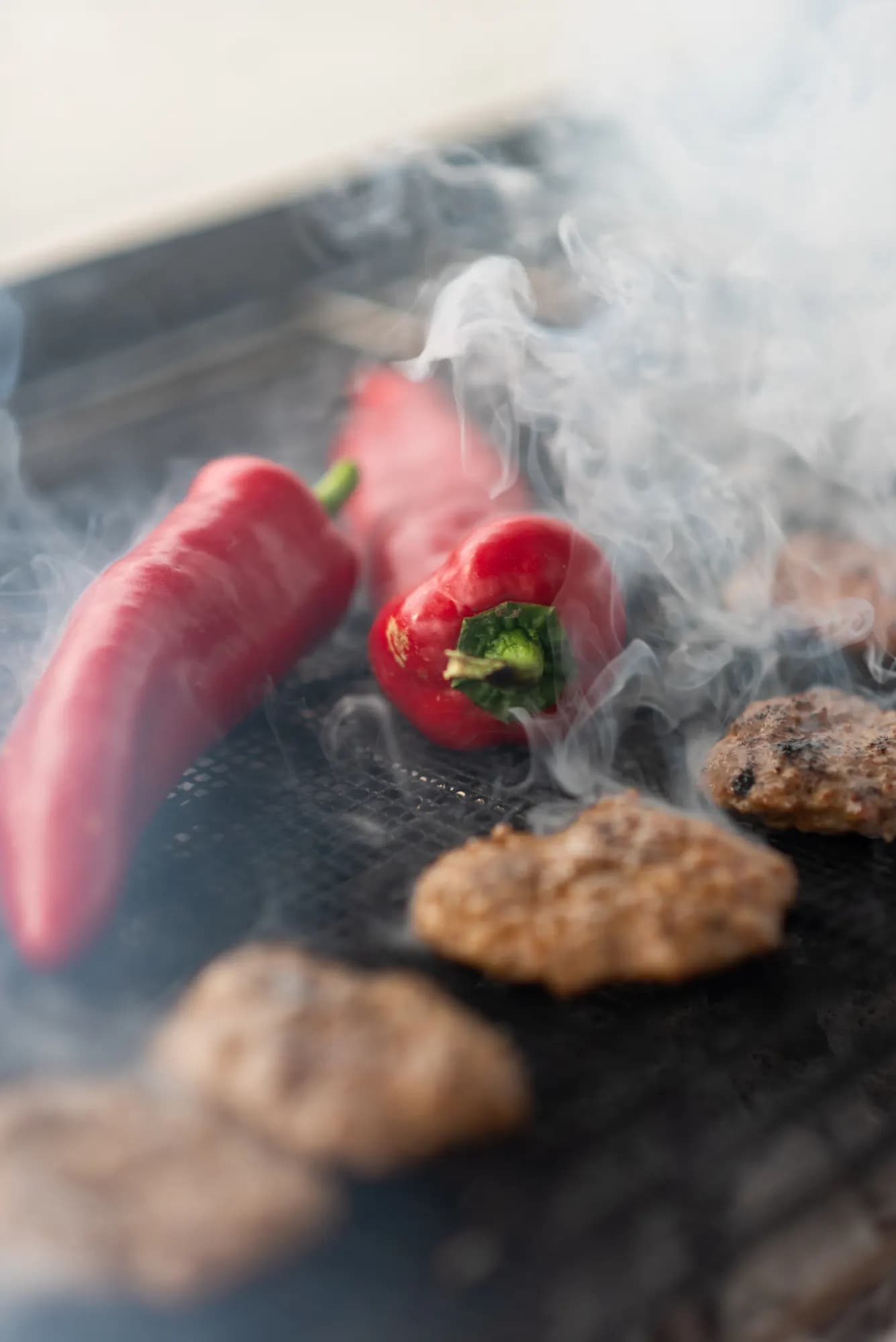 Köfte und rote Peperoni im Rauch auf dem Kohlegrill